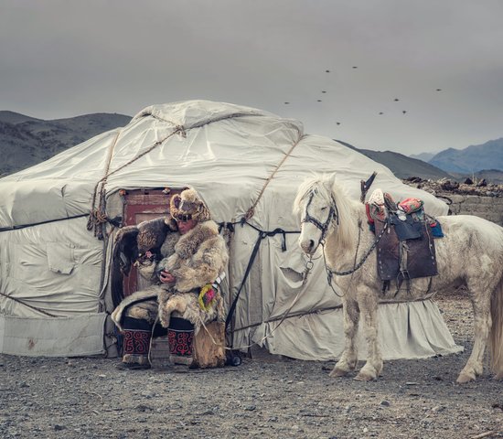Chasseur d'aigle en tenue traditionnelle devant une yourte en Mongolie