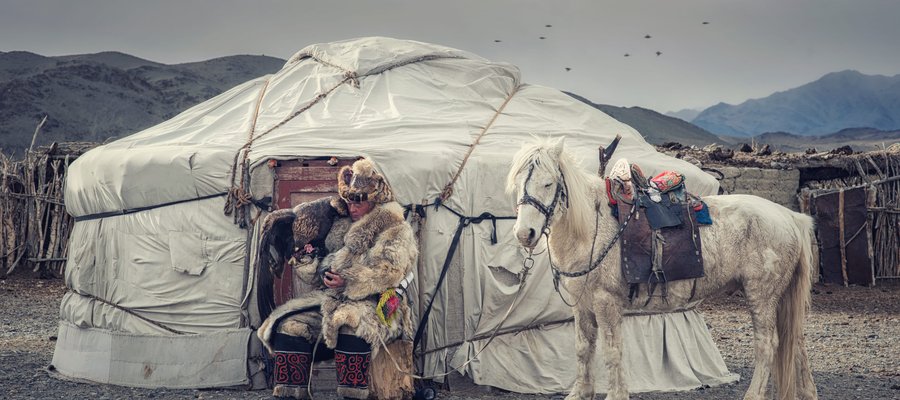 Chasseur d'aigle en tenue traditionnelle devant une yourte en Mongolie