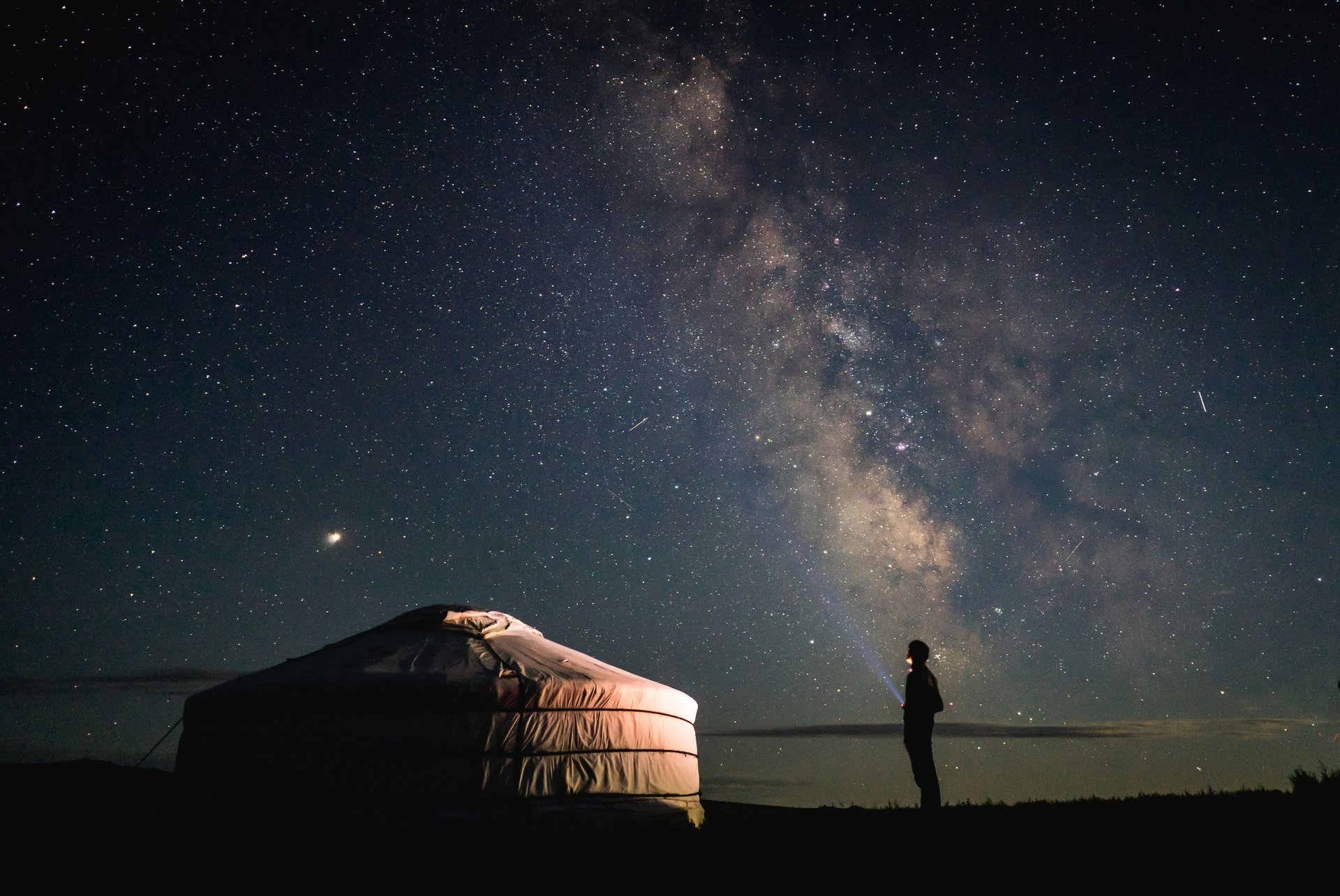 Personne debout à côté d'une tente sous un ciel étoilé en Mongolie