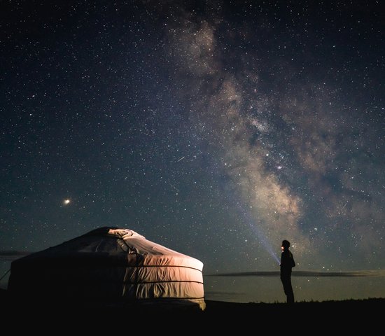 Personne debout à côté d'une tente sous un ciel étoilé en Mongolie